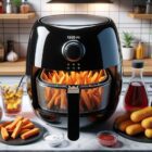 Render of a kitchen scene with a 1200x680 px resolution. Centered is a black glossy airfryer with transparent lid, allowing a glimpse of sweet potato fries and mozzarella sticks cooking inside. Surrounding the airfryer are some condiments and a glass of iced tea.